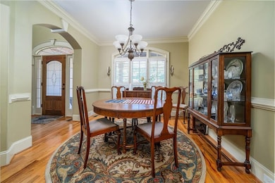 Dining space featuring a chandelier, light wood-style flooring, arched walkways, and crown molding