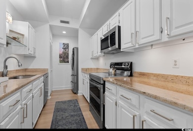 Kitchen with appliances with stainless steel finishes, light wood-type flooring, white cabinetry, light stone countertops, and recessed lighting