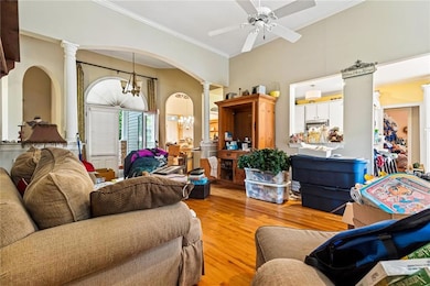 Living room with ornate columns, light wood-style floors, arched walkways, a chandelier, and ornamental molding