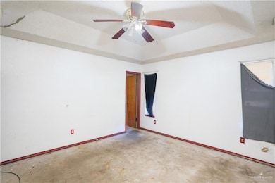 Main bedroom with a tray ceiling, unfinished concrete flooring, and ceiling fan