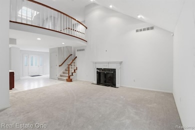 Unfurnished living room with high vaulted ceiling, recessed lighting, a fireplace, carpet floors, and stairs
