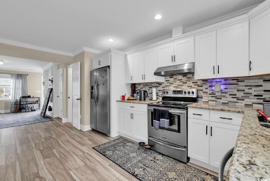 Kitchen with ornamental molding, appliances with stainless steel finishes, light stone countertops, and white cabinets