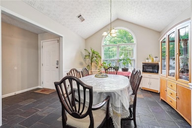 Dining room featuring vaulted ceiling, a textured ceiling, stone tile floors, and a chandelier
