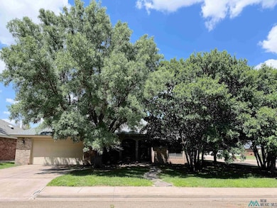 View of property hidden behind natural elements featuring brick siding, an attached garage, driveway, and a front yard