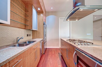 This modern kitchen features sleek wooden cabinetry, granite countertops, and a stainless steel gas cooktop. The space is well-lit with recessed lighting, a double sink, and ample storage. Ideal for contemporary living.