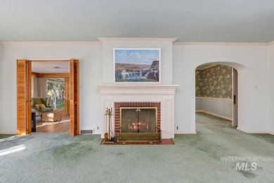 Unfurnished living room with crown molding, carpet flooring, a fireplace, arched walkways, and wallpapered walls