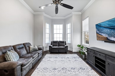Living room featuring ornamental molding, dark wood-type flooring, and ceiling fan