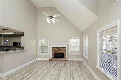 Unfurnished living room featuring high vaulted ceiling, light wood-style floors, a ceiling fan, a stone fireplace, and a sink