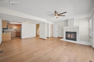 Unfurnished living room with light wood-style flooring, a stone fireplace, a ceiling fan, and a textured ceiling