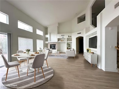 Dining room featuring a towering ceiling, a tile fireplace, light wood-style flooring, and arched walkways