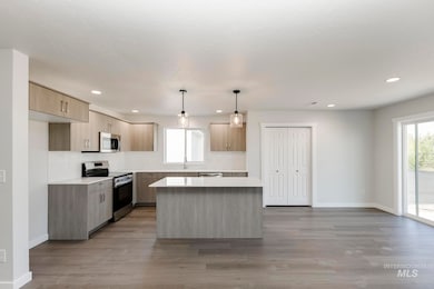 Kitchen with stainless steel appliances, modern cabinets, a center island, light brown cabinetry, and hanging light fixtures