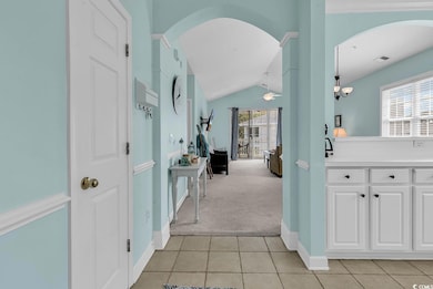 Hall with light carpet, light tile patterned flooring, arched walkways, and vaulted ceiling