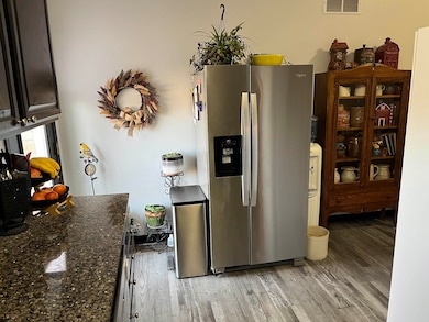 Kitchen with stainless steel fridge with ice dispenser, light wood-style flooring, and dark stone counters