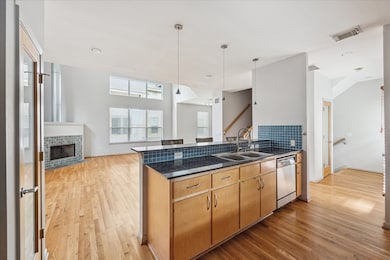 This photo showcases the open-concept kitchen and living area with hardwood floors. Large windows flood the space with natural light, while the fireplace creates a welcoming space.