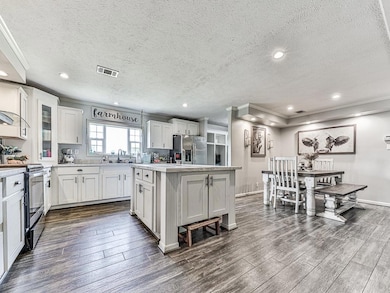 Kitchen with appliances with stainless steel finishes, ornamental molding, a kitchen island, dark wood-style floors, and a textured ceiling