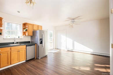 Kitchen featuring dark countertops, a ceiling fan, dark wood-type flooring, appliances with stainless steel finishes, and brown cabinets