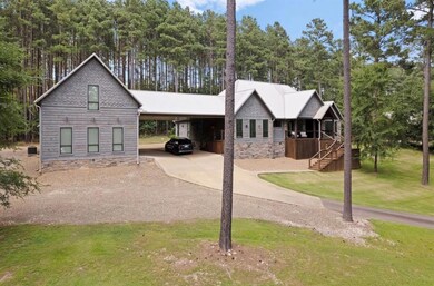View of front facade with an attached carport, driveway, a front lawn, and view of scattered trees