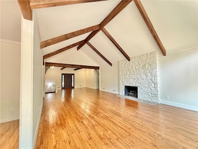 Unfurnished living room with light wood-type flooring, a stone fireplace, and baseboards