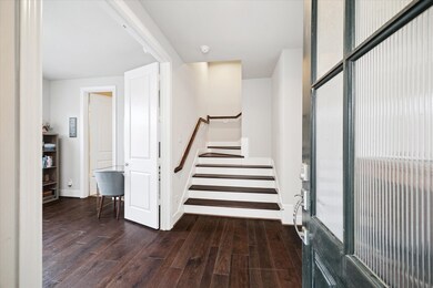 Rich wood floors and crisp white walls set a warm, modern tone as you step inside. The entry opens to a flexible first-floor room and a wide staircase, giving a welcoming sense of space and flow.
