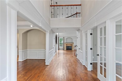 Foyer featuring french doors, wood-type flooring, a tile fireplace, wainscoting, and a high ceiling