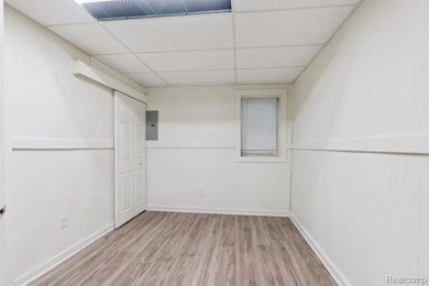 Unfurnished room featuring light wood finished floors, a drop ceiling, and electric panel