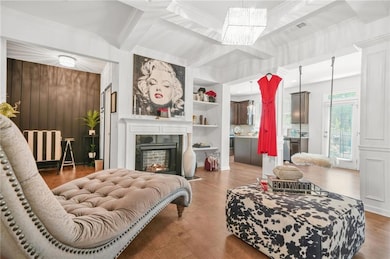 Living room with ornamental molding, wood finished floors, a chandelier, a lit fireplace, and beam ceiling
