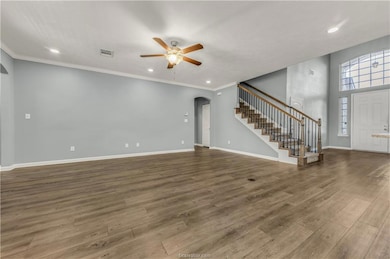 Unfurnished living room with dark wood finished floors, arched walkways, recessed lighting, ornamental molding, and stairway