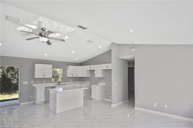 Kitchen with a kitchen island, light marble finish floors, ceiling fan, white cabinets, and high vaulted ceiling