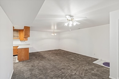 Unfurnished living room with dark colored carpet, a chandelier, and ceiling fan