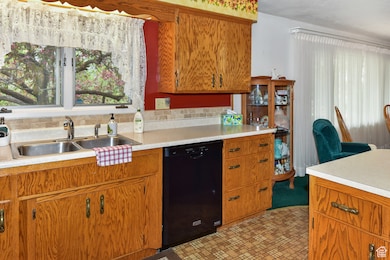 Kitchen with light countertops, brown cabinets, black dishwasher, and backsplash