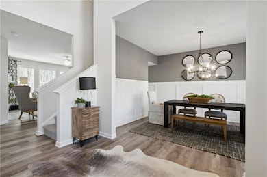 Dining space with a decorative wall, wood finished floors, stairway, a chandelier, and a wainscoted wall