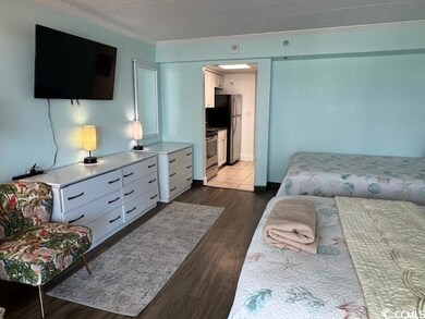Bedroom featuring crown molding, freestanding refrigerator, dark wood finished floors, and ensuite bathroom