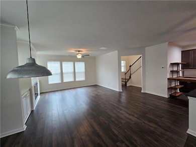 Unfurnished living room featuring stairs, plenty of natural light, crown molding, dark wood finished floors, and a ceiling fan