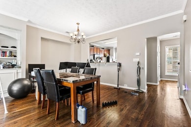 Dining room with ornamental molding, dark wood-type flooring, a textured ceiling, and a chandelier