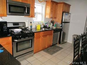 Kitchen with stainless steel appliances, light tile patterned floors, and brown cabinetry