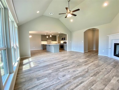 Unfurnished living room featuring ceiling fan, arched walkways, light wood-style flooring, a fireplace, and high vaulted ceiling