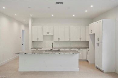 Kitchen with light stone counters, white cabinets, tasteful backsplash, recessed lighting, and an island with sink