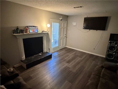 Living room featuring a textured ceiling, dark wood finished floors, and a fireplace with raised hearth