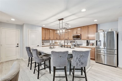 Kitchen featuring tasteful backsplash, appliances with stainless steel finishes, light countertops, recessed lighting, and an island with sink