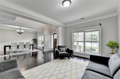 Living area featuring decorative columns, a chandelier, ornamental molding, and wood finished floors