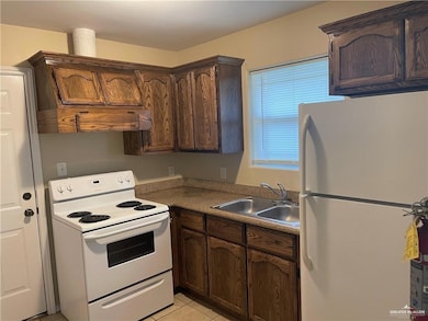 Kitchen featuring white appliances, a sink, light tile patterned floors, dark brown cabinets, and light countertops