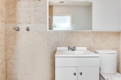 Bathroom featuring vanity, tiled shower, and tile walls