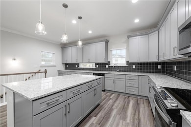 Kitchen featuring gray cabinets, pendant lighting, a center island, light stone countertops, and ornamental molding