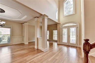 Entrance foyer with crown molding, french doors, light wood finished floors, a chandelier, and ornate columns