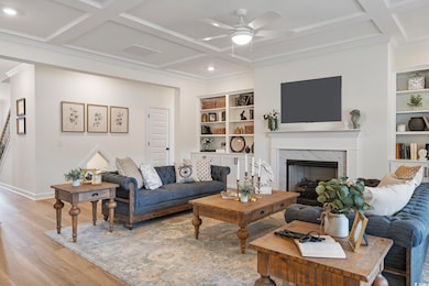 Living area with coffered ceiling, light wood-style floors, a high end fireplace, ceiling fan, and crown molding