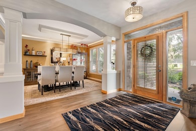 Step into a grand, light-filled foyer featuring gleaming hardwood floors, a stately front door with glass panels, and elegant sightlines into the formal dining room and living areas—setting the tone for the home’s refined yet welcoming design.