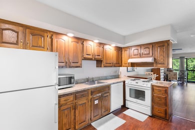 Kitchen featuring white appliances, a sink, under cabinet range hood, light countertops, and brown cabinetry