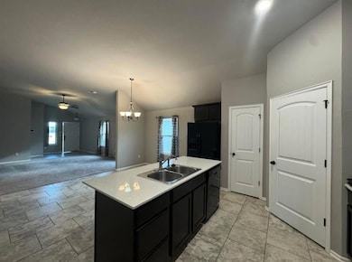 Kitchen featuring dark cabinets, black appliances, open floor plan, decorative light fixtures, and lofted ceiling