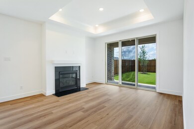 Unfurnished living room with a tray ceiling, light wood finished floors, a glass covered fireplace, recessed lighting, and baseboards