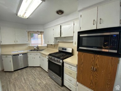 Kitchen with appliances with stainless steel finishes, white cabinets, light countertops, light wood-style flooring, and open shelves